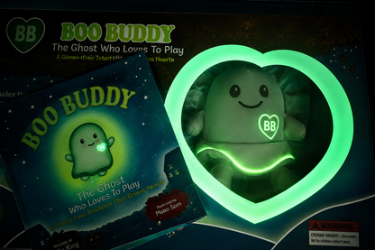 A boxed children's toy set labeled BOO BUDDY, showing a plush ghost figure inside a glowing heart-shaped frame and a matching book or booklet. 