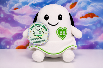 A white plush toy shaped like a smiling ghost, a green heart patch with 'BB' on the chest, and a round silver-bordered tag reading 'FIRST GLOW FRIEND,' set against a colorful cloud-like backdrop.