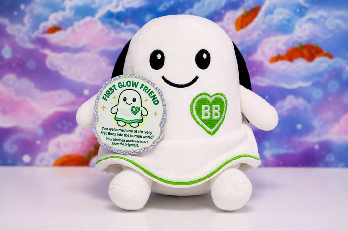 A white plush toy shaped like a smiling ghost, a green heart patch with 'BB' on the chest, and a round silver-bordered tag reading 'FIRST GLOW FRIEND,' set against a colorful cloud-like backdrop.