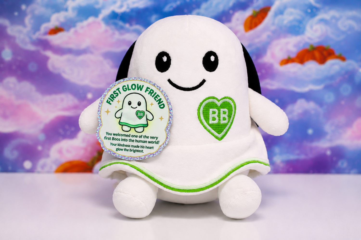 A white plush toy shaped like a smiling ghost  a green heart patch with 'BB' on the chest, and a round silver-bordered tag reading 'FIRST GLOW FRIEND,' set against a colorful cloud-like backdrop.